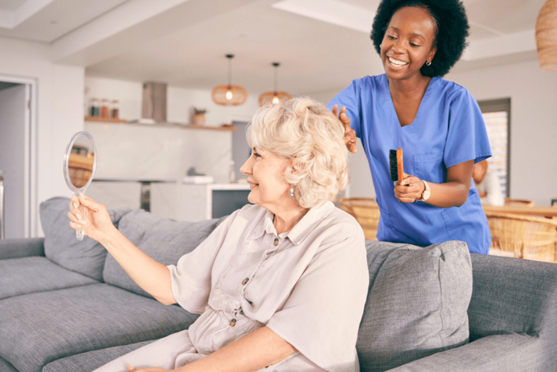 Caregiver brushing an older woman’s hair in a bright living room.